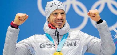 Aufnahme von Arndt Peiffer den Olympiasieger von 2018 im Biathlon. Er jubelt, hebt beide Beide nach oben und freut sich über seine Medaille.