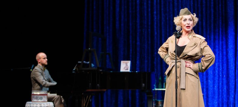 Bild einer Gesangseinlage von dem Theaterstück "The Kraut". Ein Mann spielt Klavier und eine Frau singt dazu. 