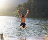 Kind springt ins Wasser ein Kind springt mit ausgestreckten Armen nach oben in einen Teich