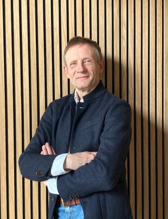 Her Dr. Brunner, an eine Wand gelehnt, mit verschränkten Armen